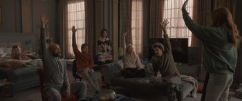 Movie still from “The Bubble” (2022), directed by Judd Apatow – A group of people sitting in a living room with their hands raised; Wide shot, High angle