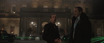 Movie still from “The Bubble” (2022), directed by Judd Apatow – A man in a suit and tie standing in front of a building at night; Medium shot, Low angle