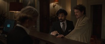 Movie still from “The Bubble” (2022), directed by Judd Apatow – A man sitting at a bar wearing a suit and tie; Medium shot, Over the shoulder angle