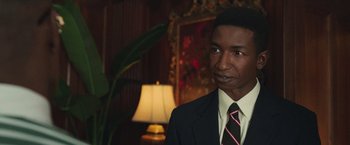 Movie still from “The Burial” (2023), directed by Maggie Betts – A man wearing a suit and tie standing in front of a lamp; Close Up shot, Over the shoulder angle