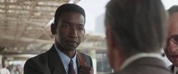 Movie still from “The Burial” (2023), directed by Maggie Betts – A man in a suit and tie holding a bag; Close Up shot, Over the shoulder angle