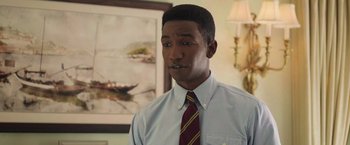 Movie still from “The Burial” (2023), directed by Maggie Betts – A man wearing a tie standing in front of a painting; Close Up shot, Low angle