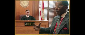 Movie still from “The Burial” (2023), directed by Maggie Betts – A man in a suit is speaking in front of a judge in a courtroom; Medium shot, Over the shoulder angle
