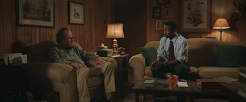 Movie still from “The Burial” (2023), directed by Maggie Betts – Two people sitting in a living room talking to each other; Medium shot, Over the shoulder angle