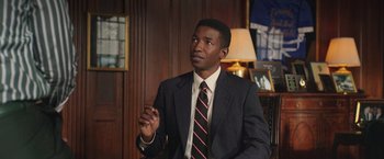 Movie still from “The Burial” (2023), directed by Maggie Betts – A man wearing a suit and tie in a room; Medium shot, High angle