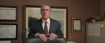 Movie still from “The Burial” (2023), directed by Maggie Betts – An older man wearing a suit and tie in front of a painting; Medium shot, Low angle