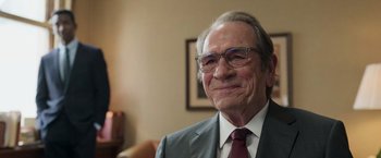 Movie still from “The Burial” (2023), directed by Maggie Betts – An older man wearing glasses and a suit and tie; Close Up shot, Over the shoulder angle