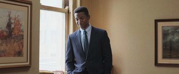 Movie still from “The Burial” (2023), directed by Maggie Betts – A man in a suit and tie standing in front of a window; Medium shot, Low angle