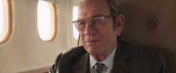 Movie still from “The Burial” (2023), directed by Maggie Betts – An older man wearing glasses and a suit; Close Up shot, Over the shoulder angle
