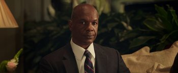 Movie still from “The Burial” (2023), directed by Maggie Betts – A man wearing a suit and tie in front of some plants; Close Up shot, Low angle