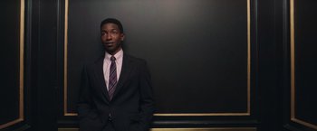 Movie still from “The Burial” (2023), directed by Maggie Betts – A man wearing a suit and tie standing in front of a wall; Medium shot, Low angle