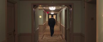 Movie still from “The Burial” (2023), directed by Maggie Betts – A man walking down a hall way in a hotel room; Wide shot, High angle