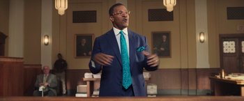 Movie still from “The Burial” (2023), directed by Maggie Betts – A man wearing a suit and tie standing in a courtroom; Medium shot, Low angle