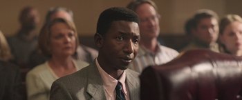 Movie still from “The Burial” (2023), directed by Maggie Betts – A man wearing a suit and tie in front of other people; Close Up shot, High angle