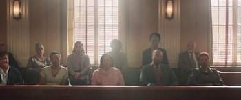 Movie still from “The Burial” (2023), directed by Maggie Betts – A group of people sitting in front of a window in a court room; Wide shot, High angle