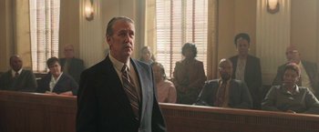 Movie still from “The Burial” (2023), directed by Maggie Betts – A man standing in front of a group of people in a court room; Medium shot, Low angle