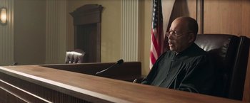 Movie still from “The Burial” (2023), directed by Maggie Betts – A judge sitting in front of a microphone in a courtroom; Medium shot, Low angle