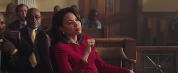Movie still from “The Burial” (2023), directed by Maggie Betts – A woman in a red dress sitting in front of a group of people; Medium shot, Over the shoulder angle
