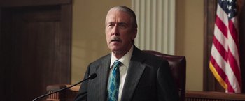 Movie still from “The Burial” (2023), directed by Maggie Betts – A man in a suit and tie sitting in a chair; Close Up shot, Low angle