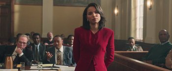 Movie still from “The Burial” (2023), directed by Maggie Betts – A woman in a red suit standing in front of other people; Medium shot, Low angle