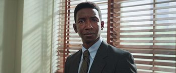 Movie still from “The Burial” (2023), directed by Maggie Betts – A man wearing a suit and tie in front of a window; Close Up shot, Low angle