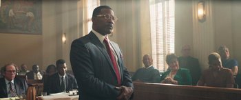 Movie still from “The Burial” (2023), directed by Maggie Betts – A man in a suit in a court room; Medium shot, Low angle