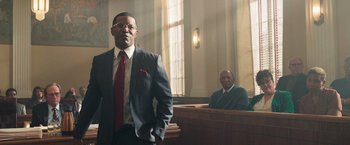 Movie still from “The Burial” (2023), directed by Maggie Betts – A man in a suit standing in front of a judge in a courtroom; Medium shot, Low angle