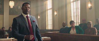 Movie still from “The Burial” (2023), directed by Maggie Betts – A man standing in front of a judge in a court room; Medium shot, Low angle