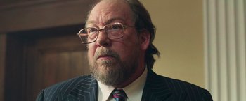 Movie still from “The Burial” (2023), directed by Maggie Betts – An older man wearing a suit and glasses; Close Up shot, Over the shoulder angle