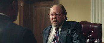 Movie still from “The Burial” (2023), directed by Maggie Betts – An older man in a suit and tie; Close Up shot, Over the shoulder angle