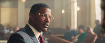 Movie still from “The Burial” (2023), directed by Maggie Betts – A person wearing a suit and glasses; Close Up shot, Low angle