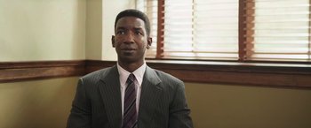 Movie still from “The Burial” (2023), directed by Maggie Betts – A man wearing a suit and tie in front of a window; Close Up shot, High angle