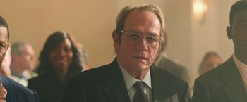 Movie still from “The Burial” (2023), directed by Maggie Betts – An older man wearing a suit and tie; Close Up shot, Over the shoulder angle