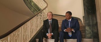 Movie still from “The Burial” (2023), directed by Maggie Betts – Two men in suits sitting on a stair case; Medium shot, Over the shoulder angle