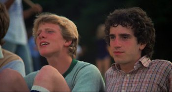 Movie still from “The Burning” (1981), directed by Tony Maylam – Two young men sitting next to each other in front of trees; Close Up shot, Low angle