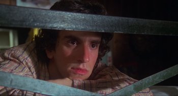 Movie still from “The Burning” (1981), directed by Tony Maylam – A young man is looking through a metal fence; Close Up shot, Low angle