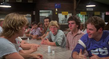 Movie still from “The Burning” (1981), directed by Tony Maylam – A group of people sitting at a table with drinks; Medium shot, Over the shoulder angle