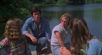 Movie still from “The Burning” (1981), directed by Tony Maylam – A group of young men sitting on the ground near a body of water; Medium shot, Over the shoulder angle