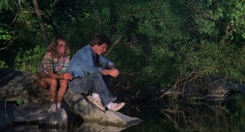 Movie still from “The Burning” (1981), directed by Tony Maylam – A man and a woman sitting on a rock near a body of water; Wide shot, High angle