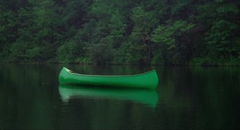 Movie still from “The Burning” (1981), directed by Tony Maylam – A green canoe floating on top of a body of water; Extreme Wide shot, High angle