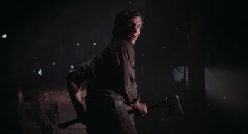 Movie still from “The Burning” (1981), directed by Tony Maylam – A man holding an axe in a dark room; Medium shot, Over the shoulder angle