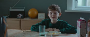 Movie still from “The Burning Sea” (2021), directed by John Andreas Andersen – A boy sitting at a table with a plate of food in front of him; Medium shot, Over the shoulder angle
