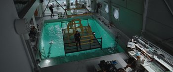 Movie still from “The Burning Sea” (2021), directed by John Andreas Andersen – A man standing in the middle of an indoor swimming pool; Extreme Wide shot, High angle