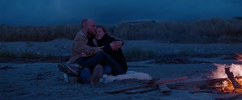 Movie still from “The Burning Sea” (2021), directed by John Andreas Andersen – A man and a woman sitting on the ground hugging; Medium shot, Low angle