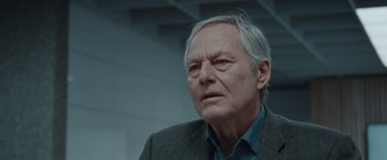 Movie still from “The Burning Sea” (2021), directed by John Andreas Andersen – An older man in a jacket and shirt looking to his left; Close Up shot, Low angle