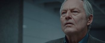 Movie still from “The Burning Sea” (2021), directed by John Andreas Andersen – An older man looking at the camera while wearing a jacket; Close Up shot, Low angle