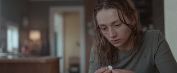 Movie still from “The Burning Sea” (2021), directed by John Andreas Andersen – A woman sitting at a table with a pill in her hand; Close Up shot, Over the shoulder angle