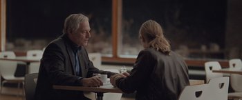 Movie still from “The Burning Sea” (2021), directed by John Andreas Andersen – An older man and a young woman sitting at a table; Medium shot, Over the shoulder angle