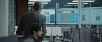 Movie still from “The Burning Sea” (2021), directed by John Andreas Andersen – Two men in a room looking at a computer screen; Medium shot, Over the shoulder angle