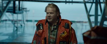 Movie still from “The Burning Sea” (2021), directed by John Andreas Andersen – A man in a life jacket standing in front of a building; Close Up shot, Over the shoulder angle